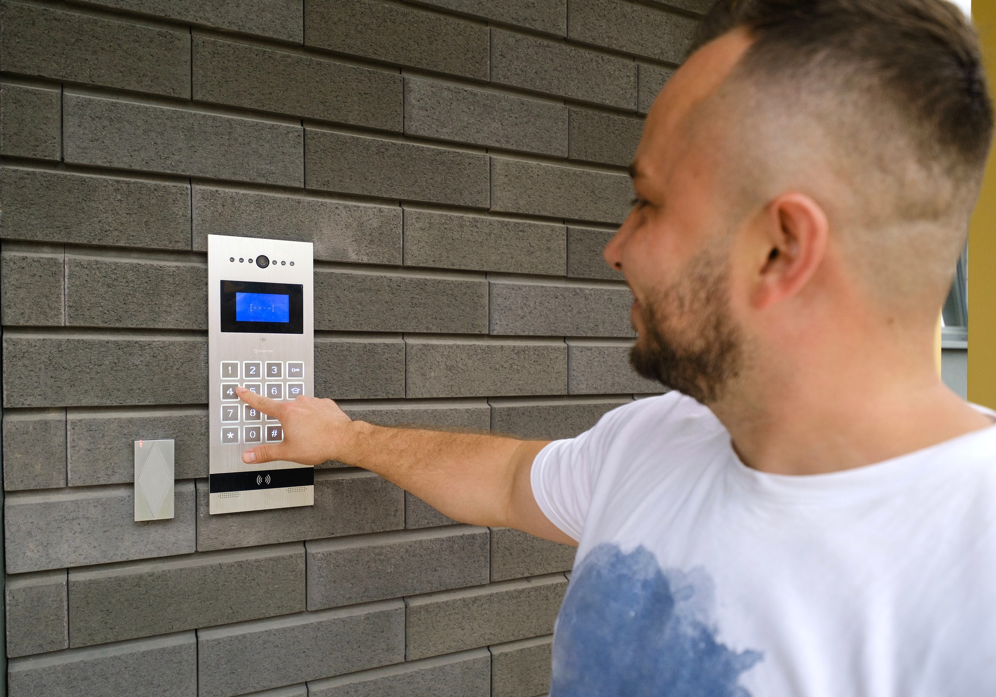 Man stands at the building of a residential building and dials the code from the intercom door.